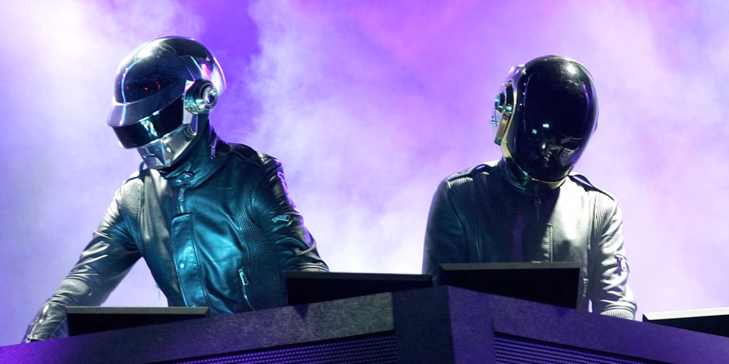 Daft Punk, wearing helmets and leather jackets, perform on stage in front of a purple-lit, smoky background. - midnightrebels.com