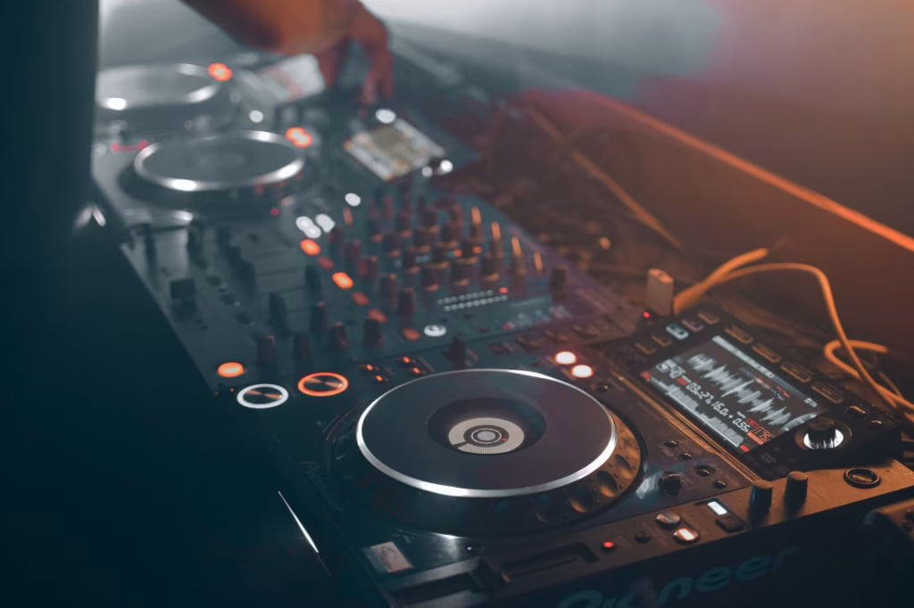 A close-up captures a dimly lit Pioneer DJ mixing console with turntables, knobs, and a waveform display, suggesting the behind-the-scenes technology driving electronic music and its potential for sustainable transformation. - midnightrebels.com