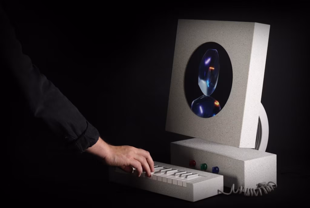 A hand plays the keyboard of the SYNTH#BOI soft synth, which features a retro computer-like design and a visualizer display, all set against a dark background. - midnightrebels.com