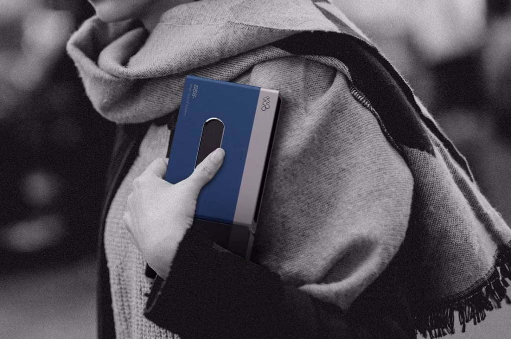 A person holds a blue smartphone dock resembling a cassette player against a background of grayscale clothing. - midnightrebels.com