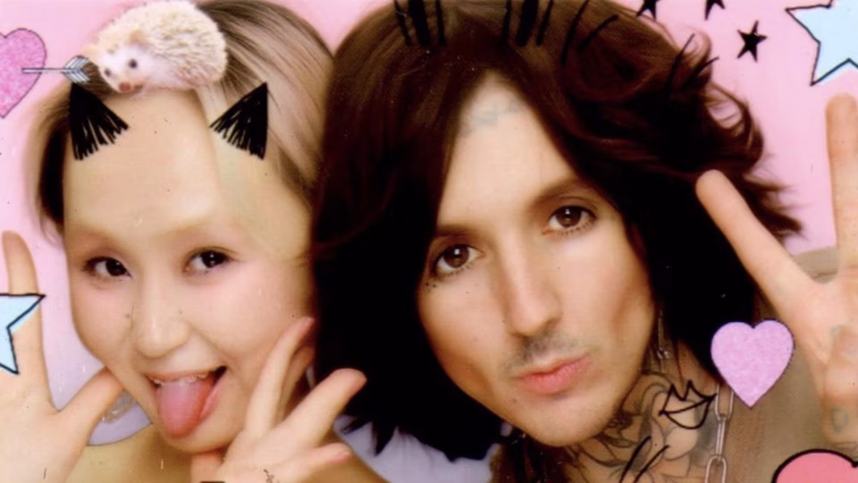 Oli Sykes and Alice Longyu Gao pose playfully with animated decorations – including a hedgehog hair accessory on GAO – in a promotional image for their 'Believe the Hype' video. - midnightrebels.com