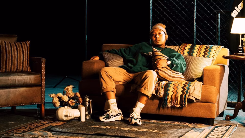 Kris Delano is pictured relaxing on a couch in a dimly lit room with vintage decor, promoting his new track "Trip Onto Unknown Grounds". - midnightrebels.com