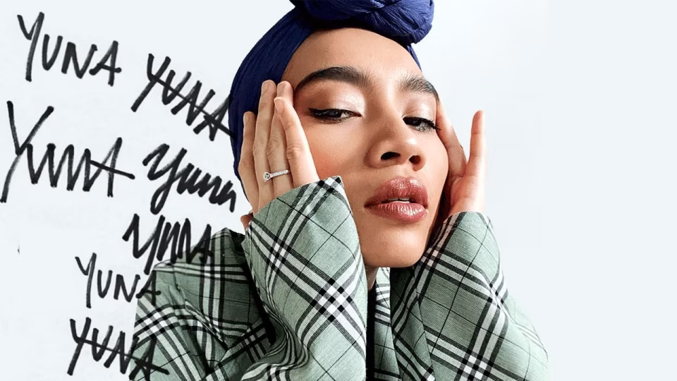 A close-up of Yuna, wearing a blue headwrap and a green plaid jacket, with her hands on her face and the word "Yuna" written repeatedly in the background. - midnightrebels.com