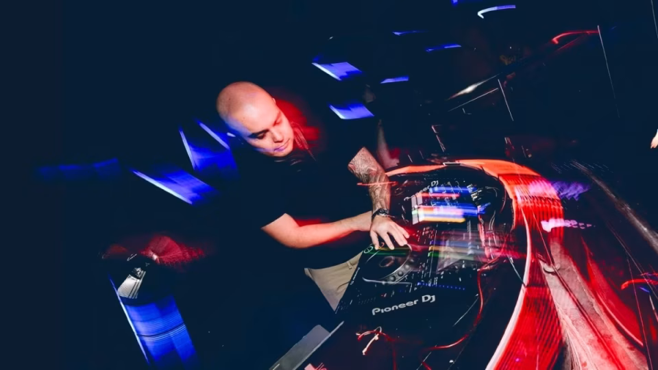 DJ Gavin Skewes is shown in a nightclub setting, mixing music on Pioneer DJ equipment amidst colorful stage lighting. - midnightrebels.com