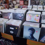 A record store display features vinyl records, including electronic music selections, categorized with dividers. - midnightrebels.com