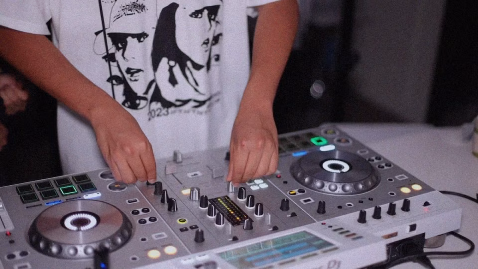A Filipino DJ with a patterned shirt adjusts the mixer controls, symbolizing the pursuit of a music career against cultural norms. - midnightrebels.com