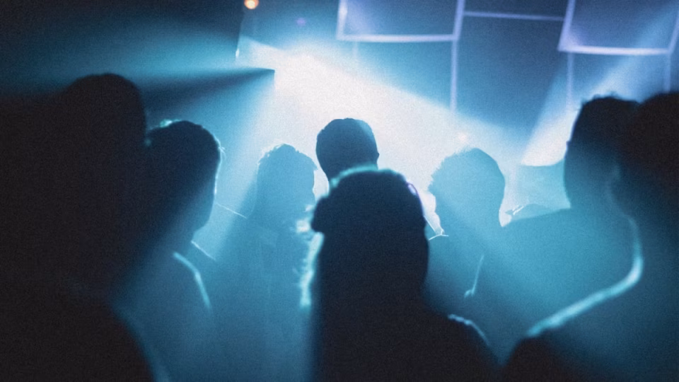 A crowd of silhouetted figures stands under bright blue stage lights at a club or concert. - midnightrebels.com