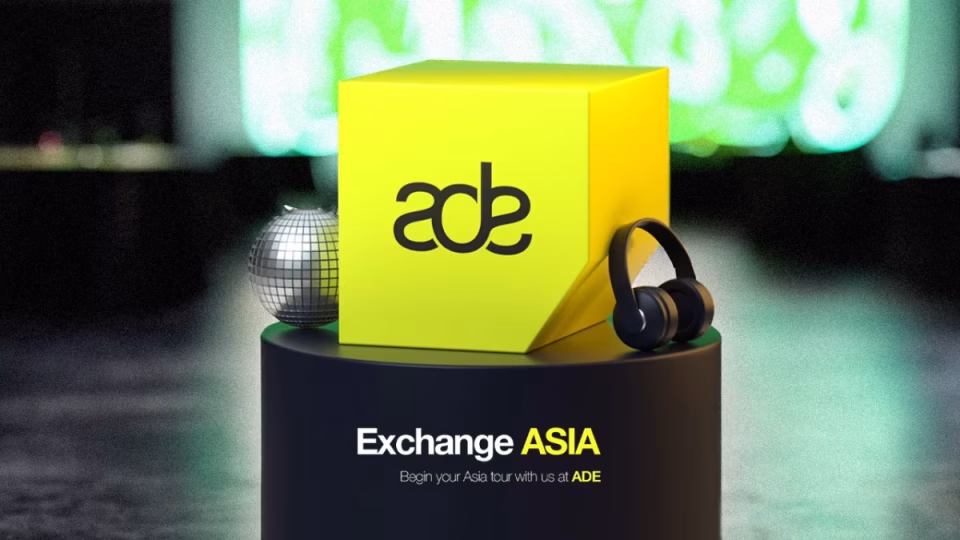 The image showcases a promotional visual for "Exchange ASIA" at ADE (Amsterdam Dance Event) with a yellow cube bearing the "ade" logo, a disco ball, and headphones atop a black pedestal. - midnightrebels.com