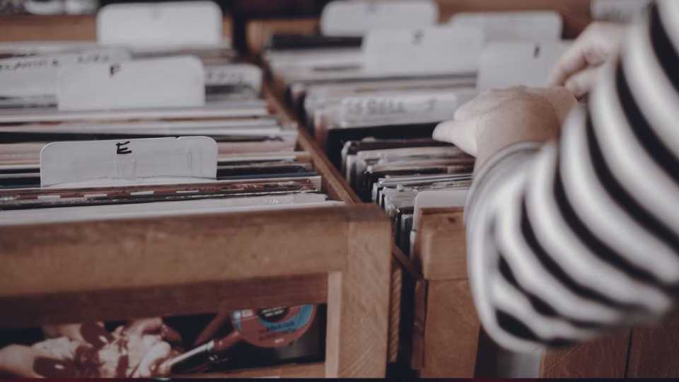 Close-up of hands browsing through a crate of vinyl records, organized alphabetically, symbolizing the dedication and curation of a traditional DJ's set. This evokes the era before digital playlists and algorithm-driven music selection. - midnightrebels.com