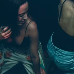 Overhead shot of young women dancing at a club with low lighting. One woman is wearing floral patterned pants and a black top, holding a drink, while another is wearing denim shorts and a black lace top. - midnightrebels.com