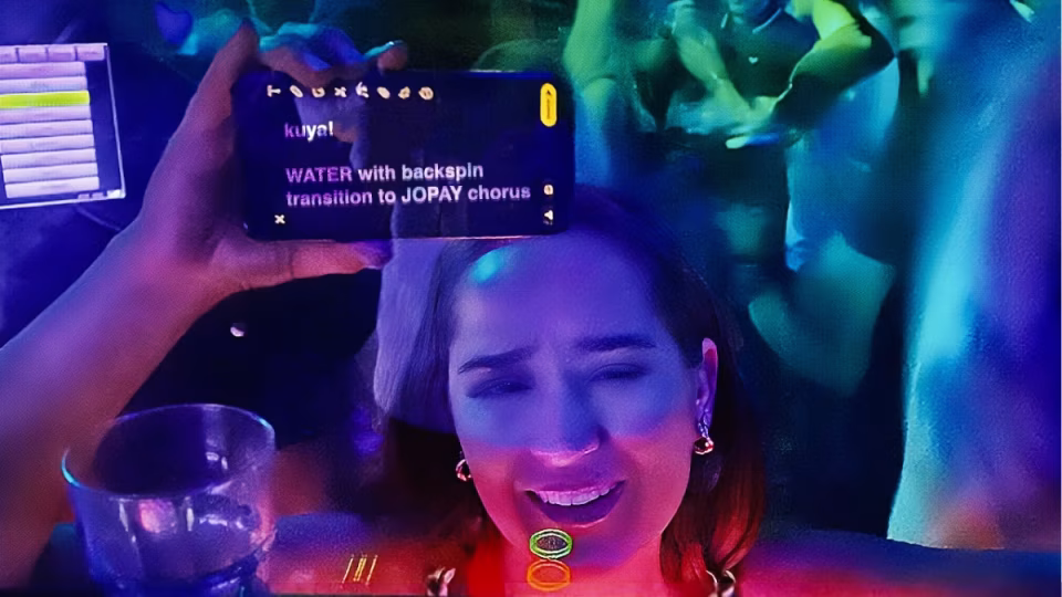 A woman at a club holds up her phone showing a complex DJ song request: "WATER with backspin transition to JOPAY chorus." This illustrates the increasing sophistication of DJ song requests in 2024. - midnightrebels.com