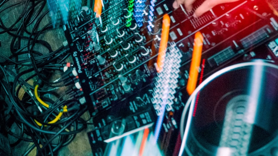 Overhead shot of a DJ mixer table with a DJ's hand adjusting the controls. Cables are visible, highlighting the complexity of the setup, emphasizing the need for fair wages and working conditions for Filipino DJs. - midnightrebels.com