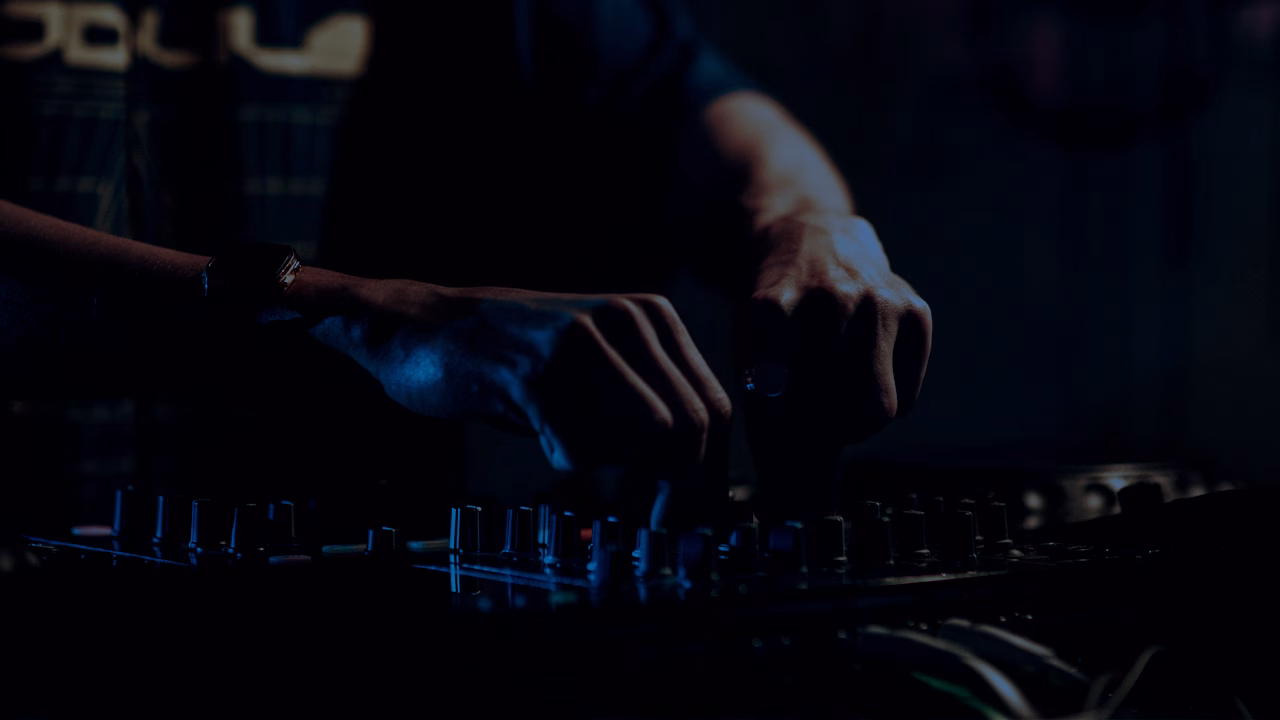 Close-up of a DJ's hands operating a mixing board under blue club lights, representing the nightlife industry impacted by a QC bar's sudden closure and unpaid wages. - midnightrebels.com