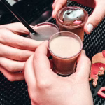 Close-up of three hands holding shot glasses filled with colorful cocktails on a bar counter with a Red Bull logo, representing potential factors influencing bar sales including drink choices and brand appeal, relevant to discussions about DJs and bar revenue. - midnightrebels.com