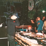 A DJ performs in a dimly lit warehouse rave, complete with graffiti art and a crowd of people dressed in unique styles, capturing the underground spirit of counter-culture nightlife. - midnightrebels.com