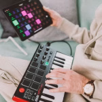 A person is shown seated, using a mini MIDI keyboard and an iPad with a music production app, illustrating the evolution of electronic dance music production. - midnightrebels.com