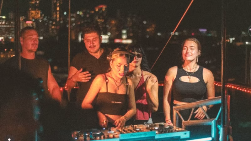 DJ Francie Gee spins at a rooftop party overlooking a city skyline, surrounded by friends enjoying the music and atmosphere. - midnightrebels.com