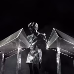 Gesaffelstein, shrouded in mystery, performs on stage behind two pyramidal metallic consoles against a stark black backdrop, illustrating his enigmatic presence in the techno scene. - midnightrebels.com