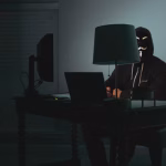 Hacker with Anonymous mask using computer in dark room.