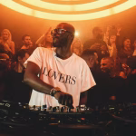 DJ Black Coffee performing live, crowd behind him in club.