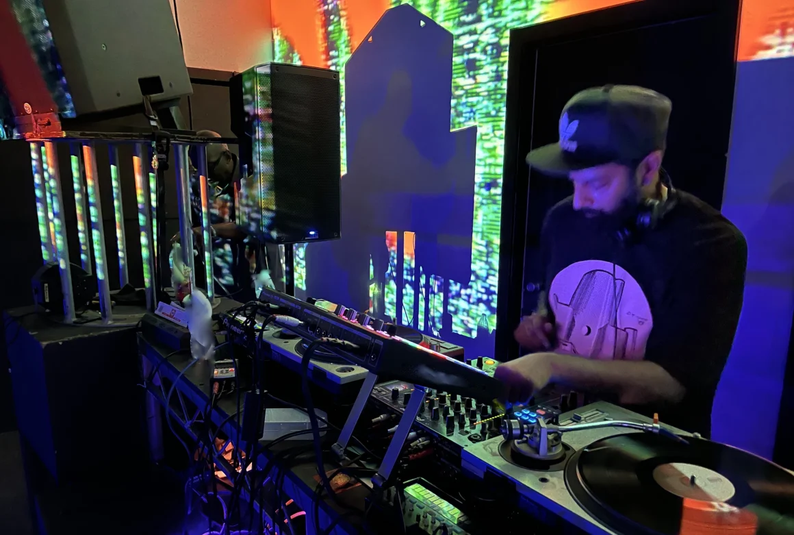 DJ spinning vinyl at nightclub, colorful lights, good music vibes.