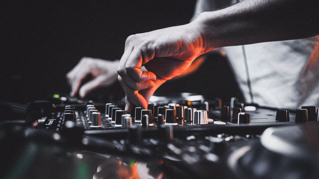 DJ mixing music with soundboard console in dark club.