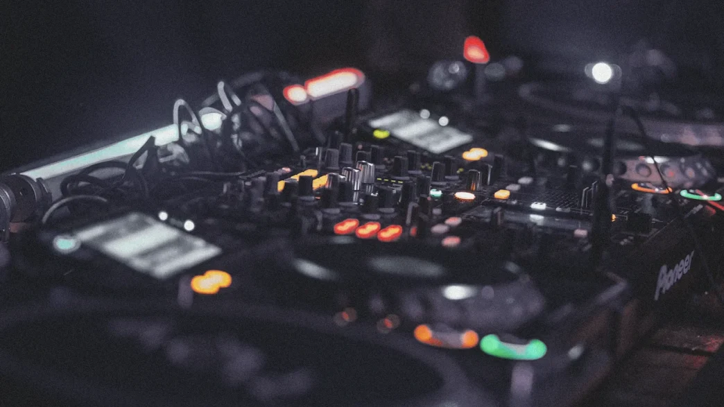 Pioneer DJ mixer board with knobs, sliders, and colorful lights.