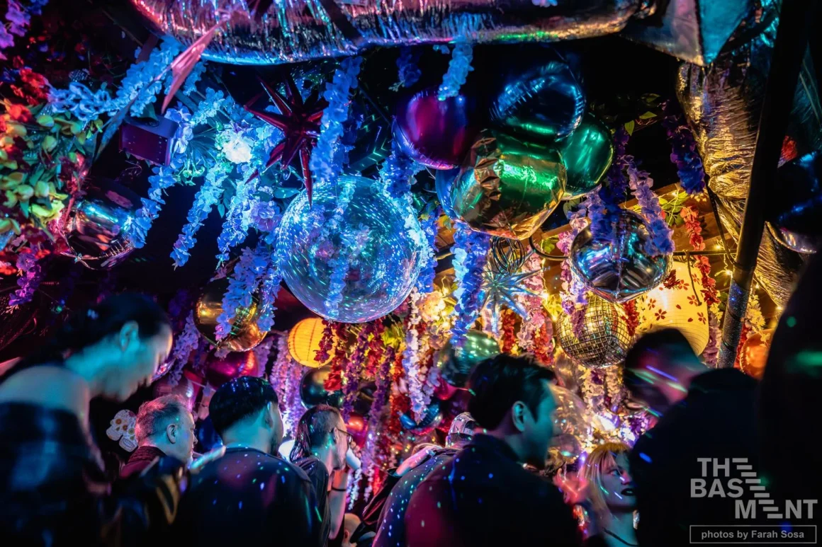 Party crowd under disco balls and colorful floral decorations.