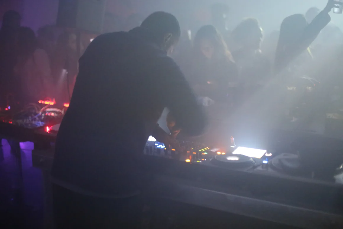 DJ performing in a smoky club with dancing crowd.