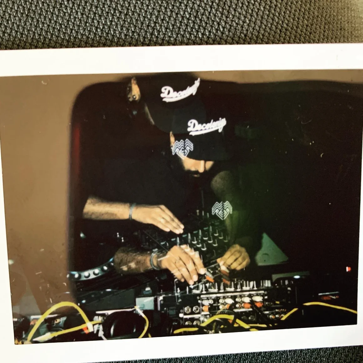 DJ using equipment, wearing a black hat and shirt.