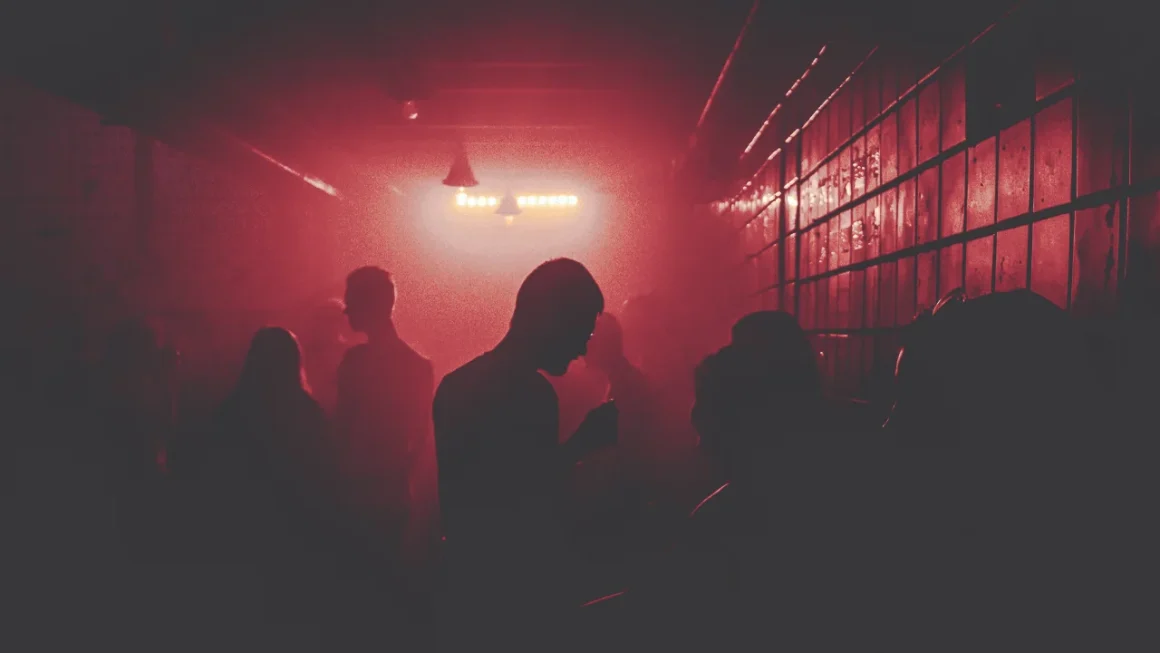 Silhouettes of dancers on red dance floor with intense strobe lighting at electronic music nightclub