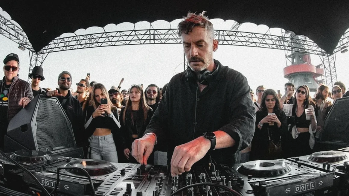 A DJ, Bonobo performing at an outdoor music event with a crowd in the background