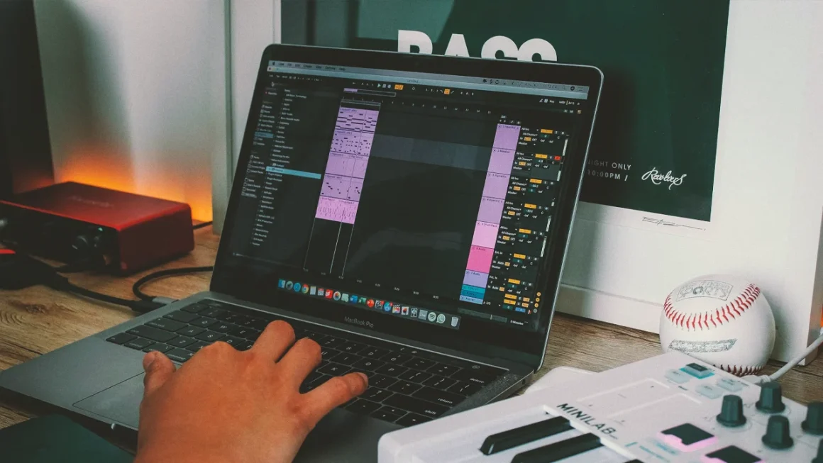 A person using music production software on a laptop in a home studio setup.