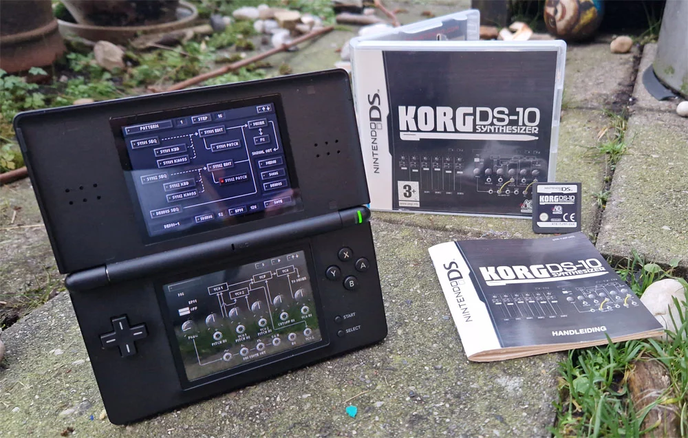 A Nintendo DS displaying the KORG DS-10 synthesizer software on its screens, with the game cartridge, manual, and the game case placed beside it on a grassy surface.