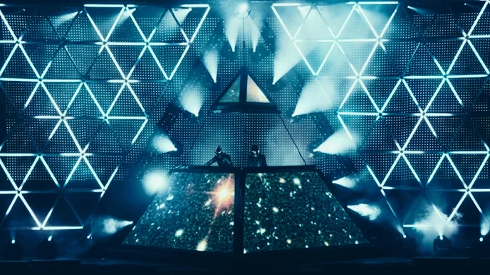 Electronic music concert stage with Daft Punk behind a pyramid-shaped LED screen and geometric light patterns