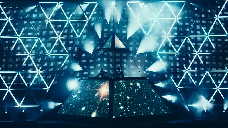 Electronic music concert stage with Daft Punk behind a pyramid-shaped LED screen and geometric light patterns