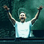 David Guetta performing with arms raised on stage in front of LED screen