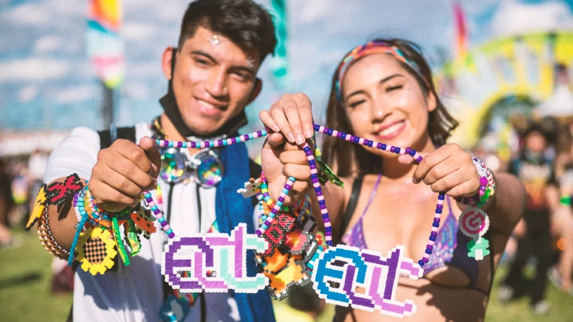 Two festival attendees smiling and holding colorful beaded necklaces with pixel art pendants