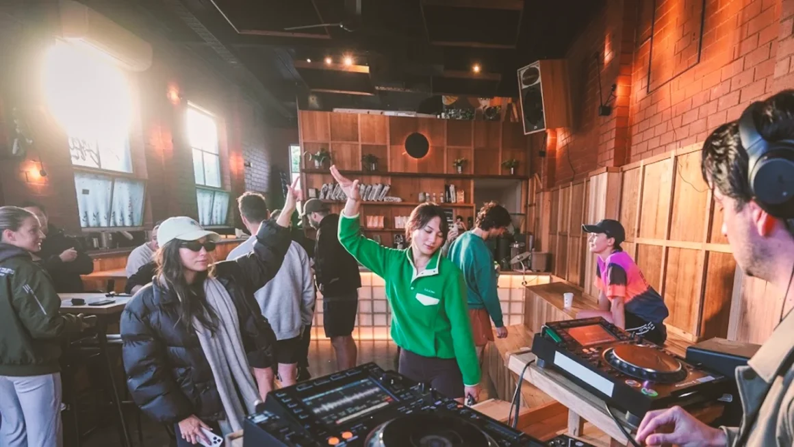 People socializing and dancing in a warmly lit indoor venue with DJ equipment in the foreground