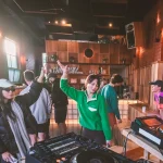 People socializing and dancing in a warmly lit indoor venue with DJ equipment in the foreground