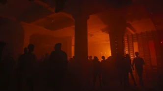 People standing and walking in a dimly lit indoor space with orange lighting and large pillars