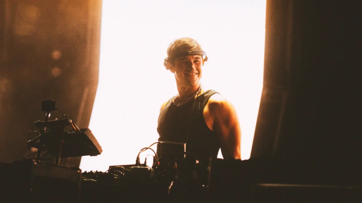 Smiling DJ in visor performing electronic music on a bright stage.