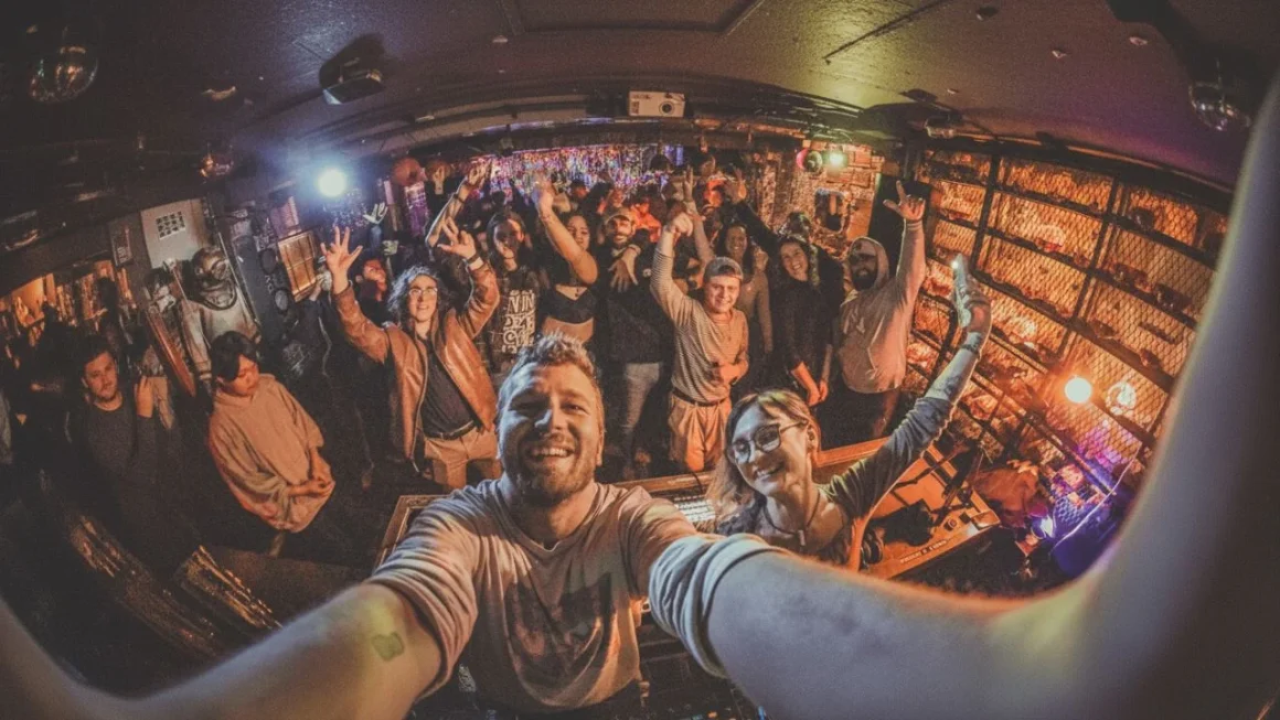 Smiling DJ and happy crowd taking a selfie at an energetic nightclub.