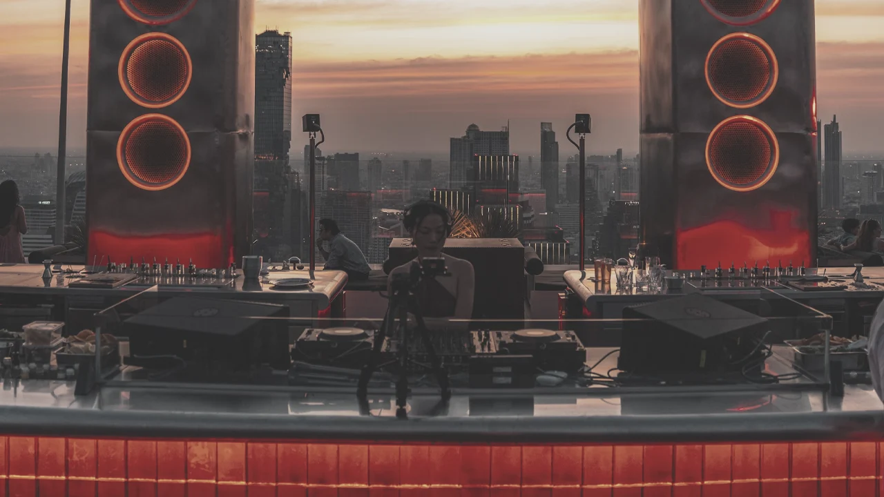 DJ performs at a stylish rooftop bar overlooking a city at sunset.