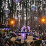 DJ with purple wings plays at vibrant forest festival, dancing crowd, holographic spheres.