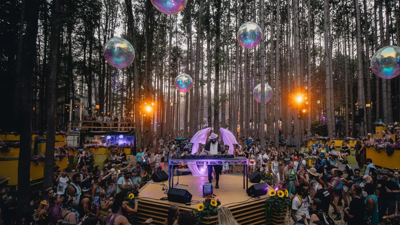DJ with purple wings plays at vibrant forest festival, dancing crowd, holographic spheres.