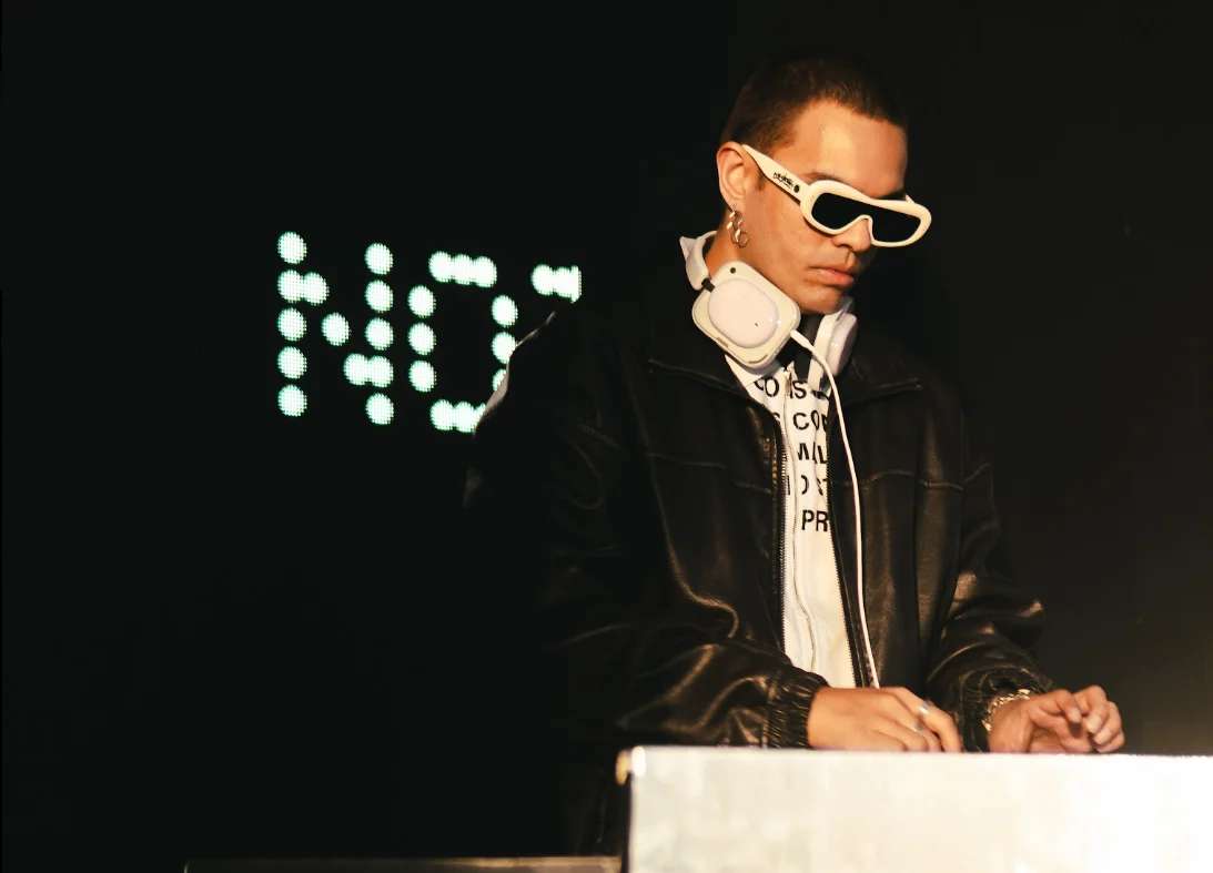 DJ with white futuristic sunglasses and headphones performing in a dark club.